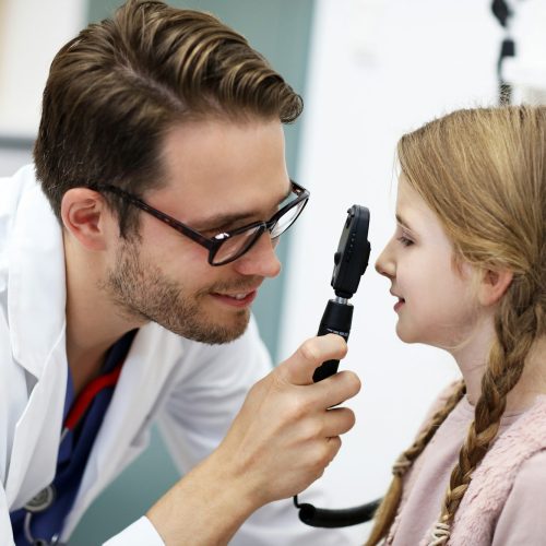 Child male optometrist examines eyesight of little girl